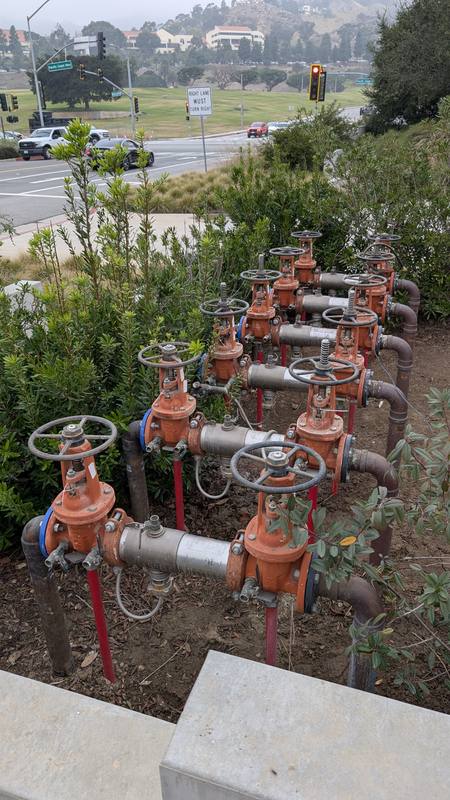 Row of red backflow preventer assemblies with gate valves in a landscaped area