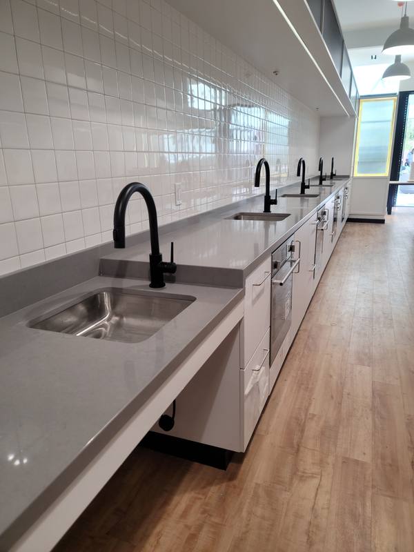 Row of black-faucet sinks along a white-tiled kitchen counter