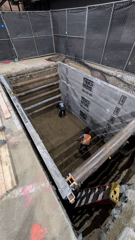 Large shored excavation surrounded by fencing, with workers at the bottom