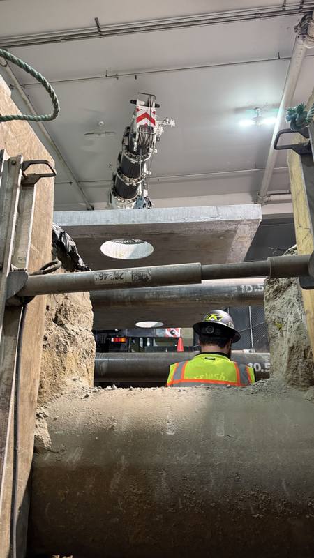 Crane rigging suspended over a deep shored trench with a worker below