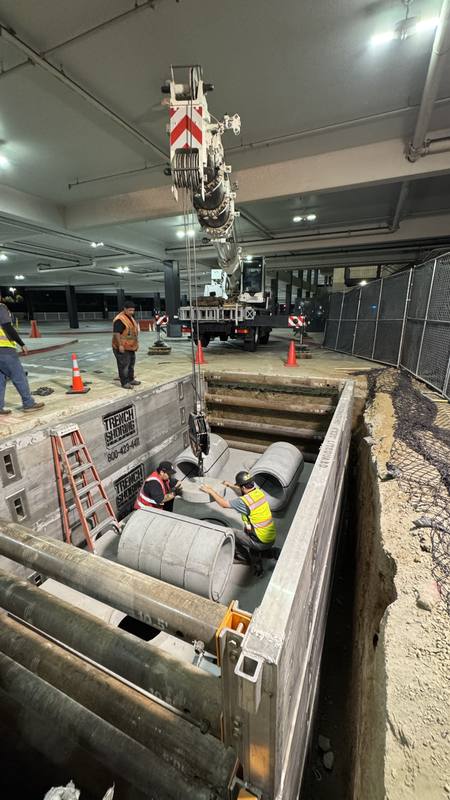 Crew members working inside a shored pit while a crane lowers precast sections