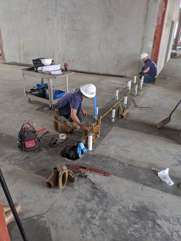 Two plumbers in hard hats installing carriers on a concrete slab