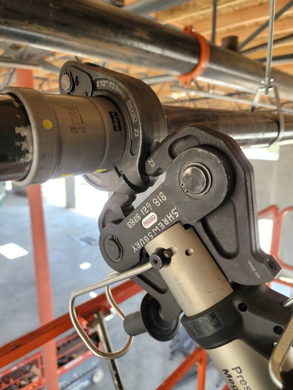 Hydraulic press tool jaws clamped on a large-diameter copper fitting