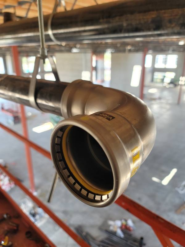 Large-diameter press-fit copper elbow hanging from overhead structure