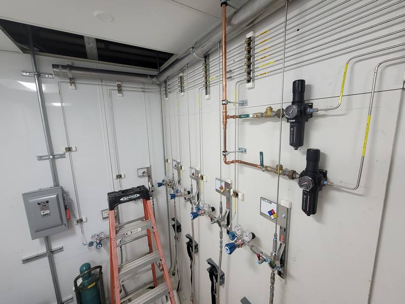 Aerospace lab gas room wall with stainless tubing, regulators and labeled outlets