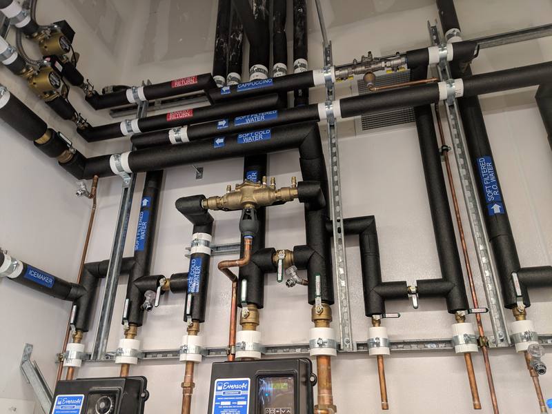 Wall of insulated hot and cold water piping with valves and pumps