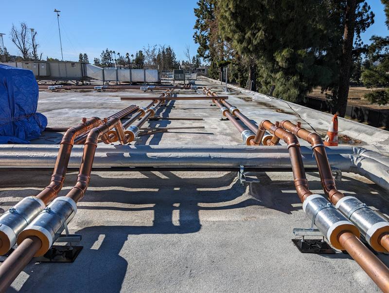 Insulated copper pipe runs on supports across a large commercial roof