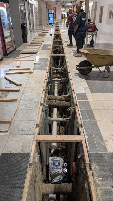 Narrow shored utility trench cut through a mall corridor floor