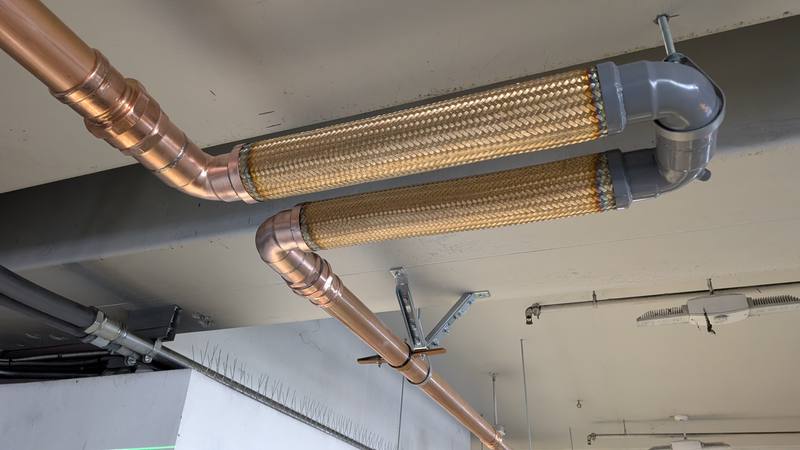 Overhead copper piping with braided flexible connectors at a structural joint