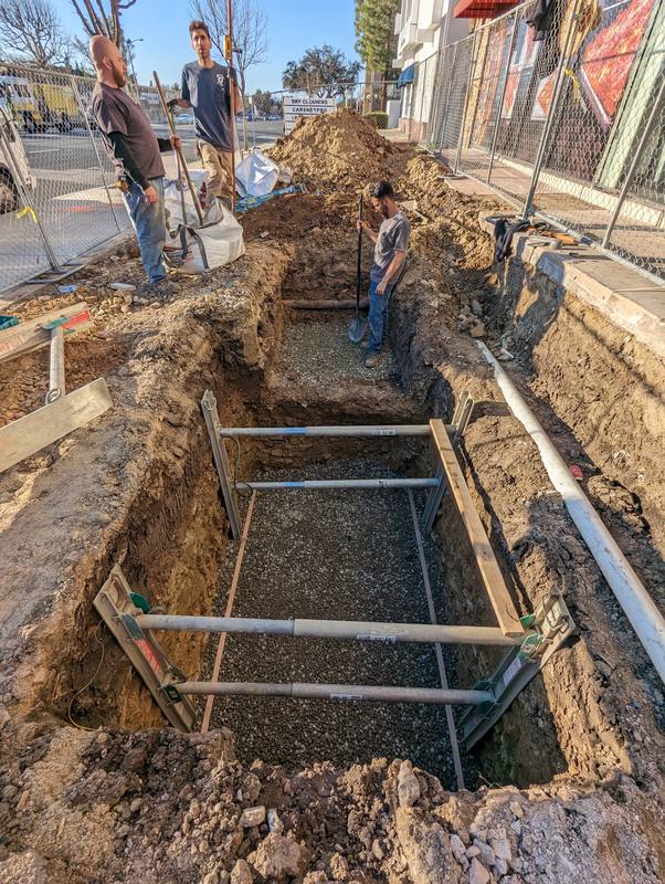 Shored utility trench along a street with crew members