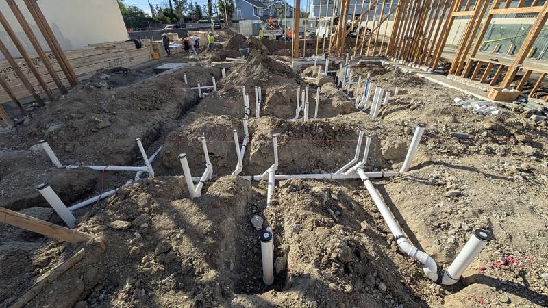 Underground PVC waste and vent rough-in in trenches inside a wood-framed building